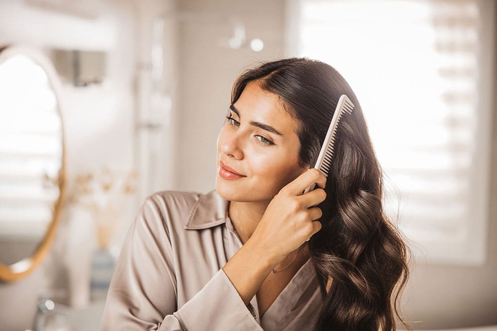 Beauty Blog Smiling young woman combing her hair in bathroom