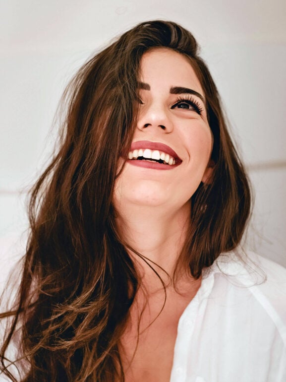 Beauty Blog Smiling woman with beautiful long brown hair after using our haircare routine for dry damaged hair, looking upward with joy.