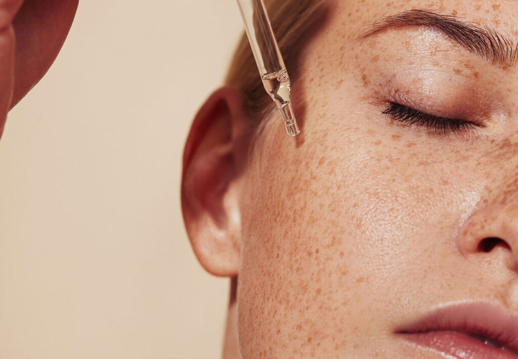 Close-up highly detailed shot of female skin with freckles and pipette with serum
