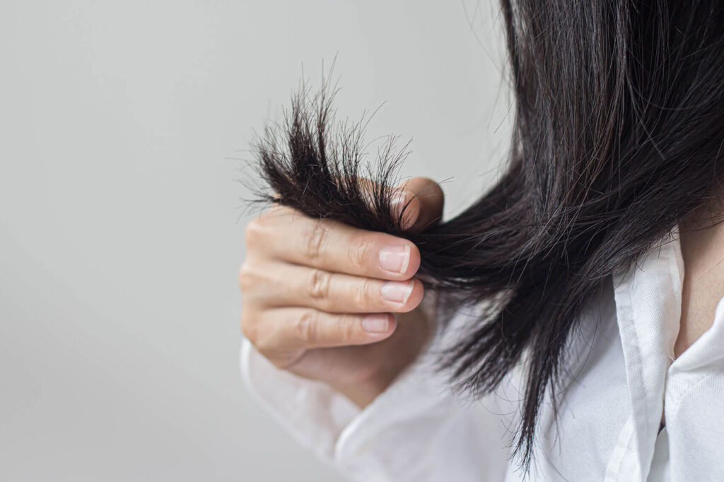 Beauty Blog woman's hand holding her long hair and looking at damaged split ends