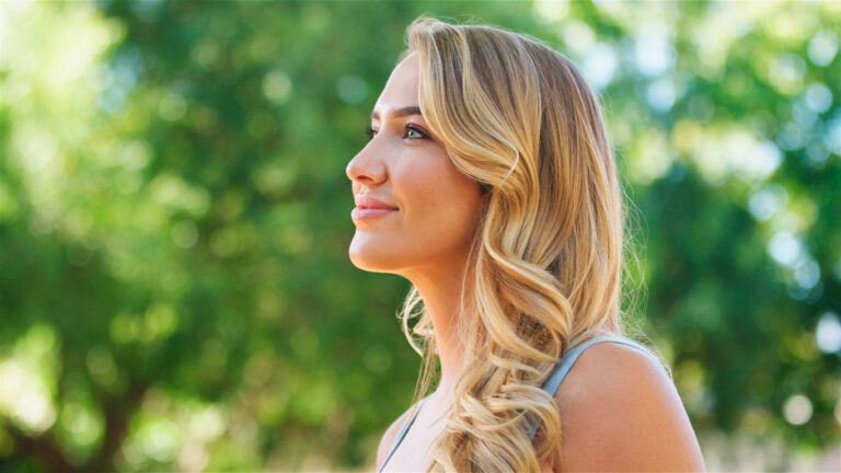 Young Woman Smiling Outdoors Under Tree Canopy on a Sunny Day