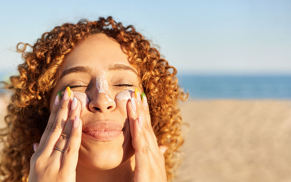 Beauty Blog Smiling happy woman applying sunscreen to her face wondering why does mineral sunscreen pill