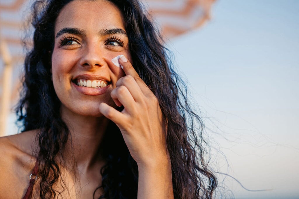 Beauty Blog Young Woman considering zinc oxide vs titanium oxide sunscreen as he os applying sunscreen On Her Face On The Beach