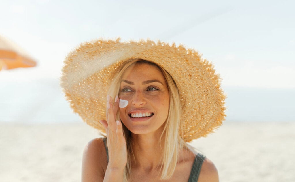 Beauty Blog Young woman applying sunscreen on her face while at the beach stock photo.jpg