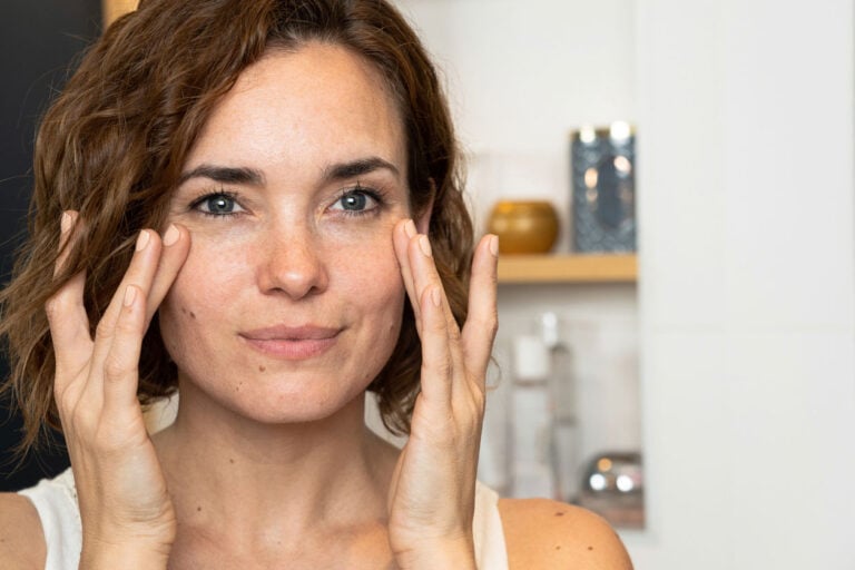 Close-up of woman applying cream to her cheeckbones using both hands