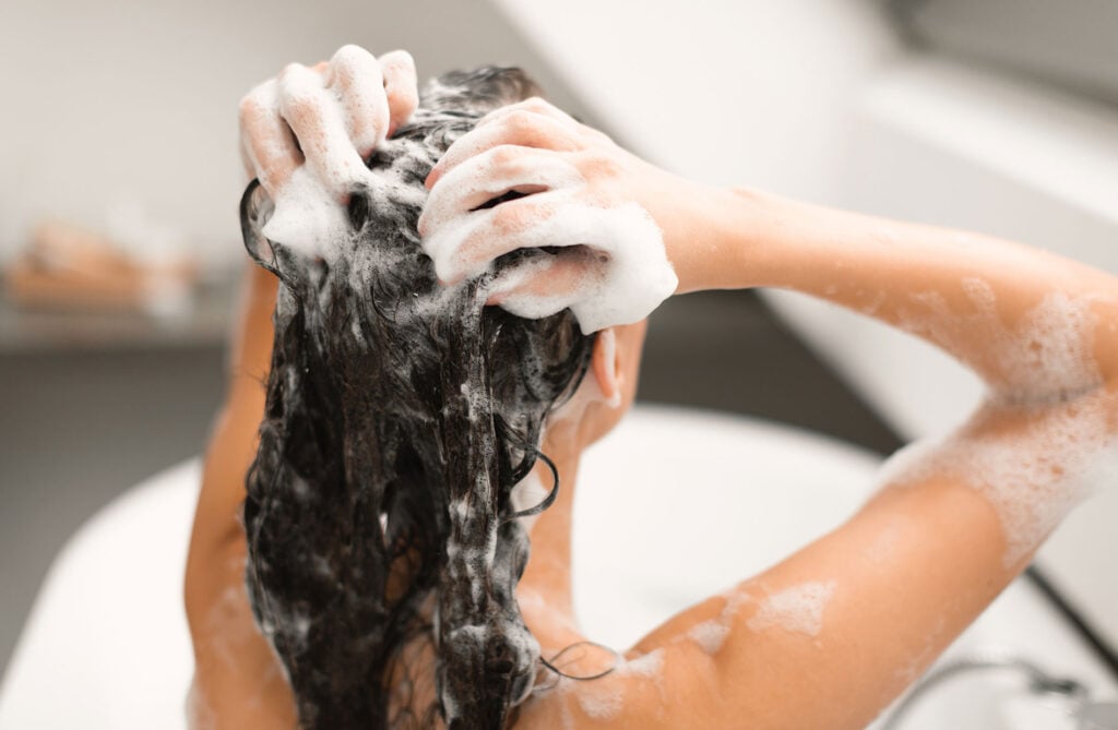 Beauty Blog Back View Of Female Applying Shampoo to think hair and considering clarifying shampoo vs regular shampoo for thick hair