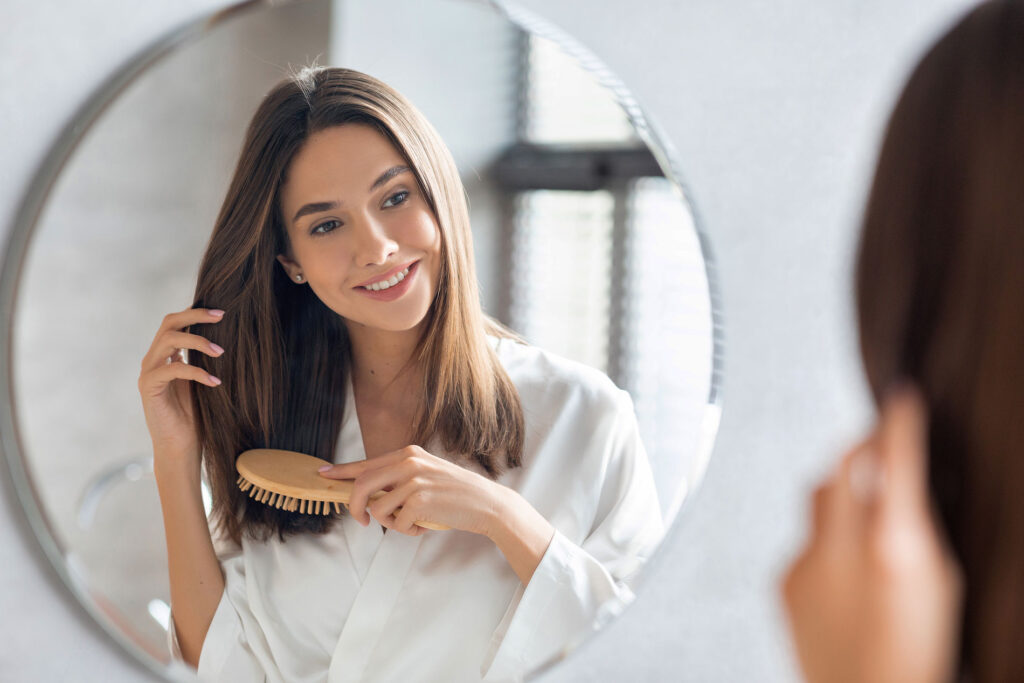Beauty Blog Haircare Concept. Attractive Young Lady Brushing Her Hair With Comb Near Mirror stock photo