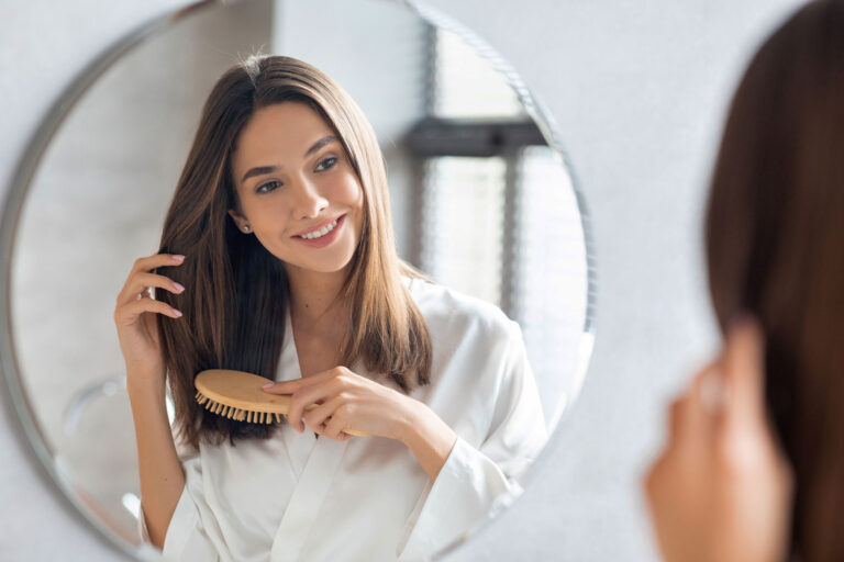 Haircare Concept. Attractive Young Lady Brushing Her Hair With Comb Near Mirror stock photo