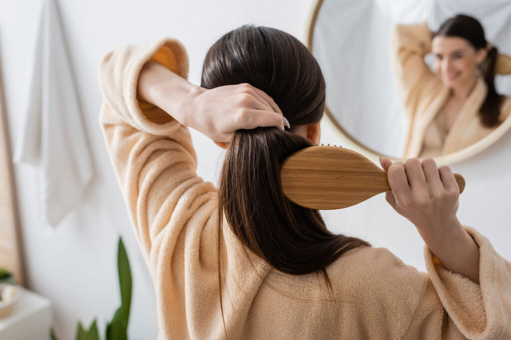 Beauty Blog back view of young brunette woman brushing hair in bathroom stock photo