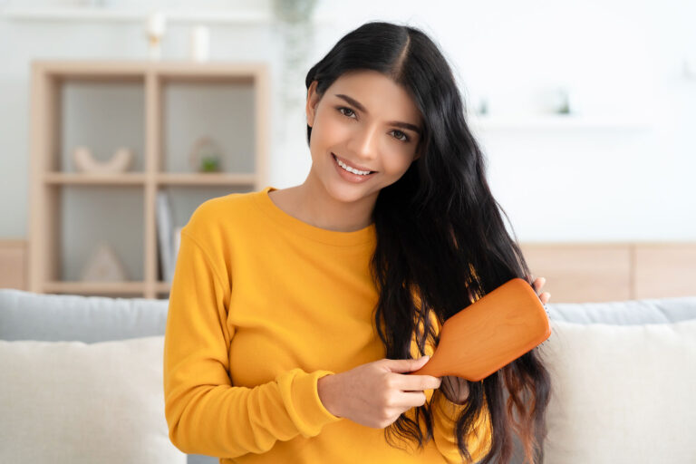woman brushing and detangling hair using wooden brush in living room at home stock photo