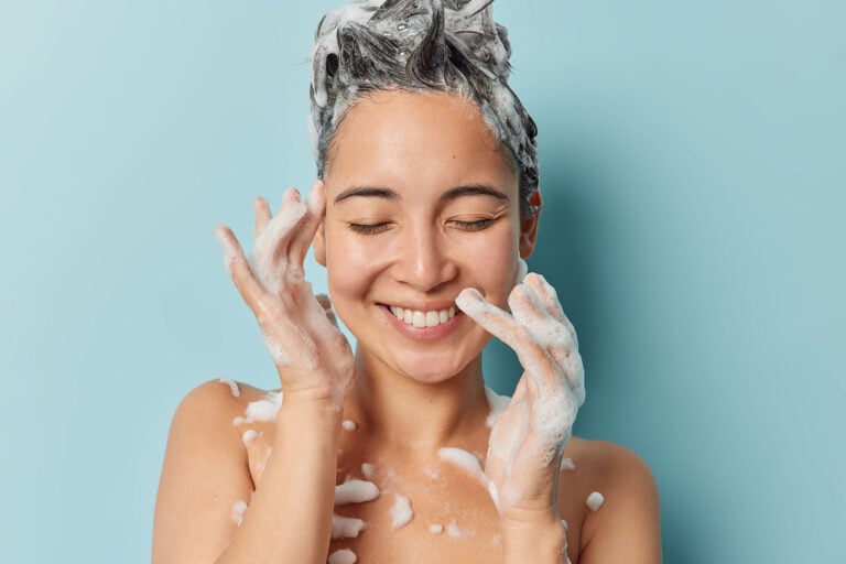 young brunette Asian woman washes hair applies shampoo stock photo