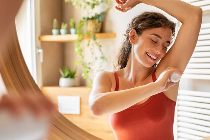 Happy young woman using roll on deodorant stock photo